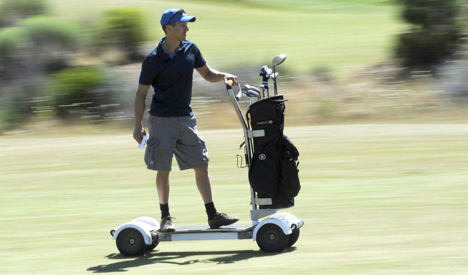 Golfer riding an all-electric GolfBoard along the fairway, clubs on the platform